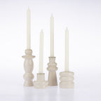 Four cream-colored taper candle holders with matching taper candles, arranged on a clean white background.