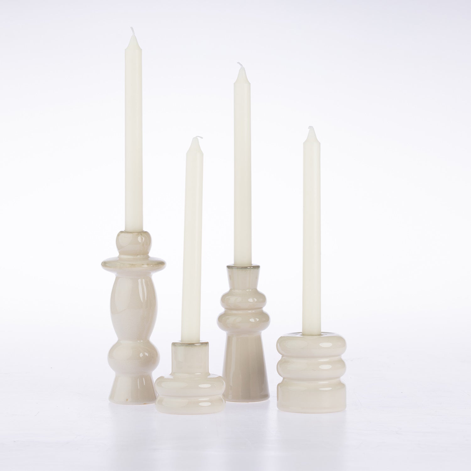 Four cream-colored taper candle holders with matching taper candles, arranged on a clean white background.