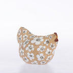 A ceramic chicken-shaped planter with a beige background, decorated with a white floral pattern and a brown comb, set against a plain white background.