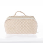 Tan quilted toiletry bag with a zip-around closure and top carry handle on a white background.