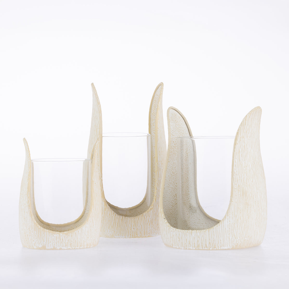 Three ivory textured candle holders in varying sizes with curved sculptural frames and clear glass inserts.