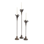 Set of three antique bronze metal candle holders in varying heights with white taper candles and decorative leaf-shaped tops.