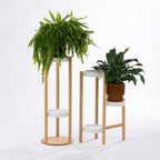 Two contemporary bamboo and white planter stands of different heights showcase lush indoor plants, creating a fresh, layered display that adds natural warmth and modern style to any living space.