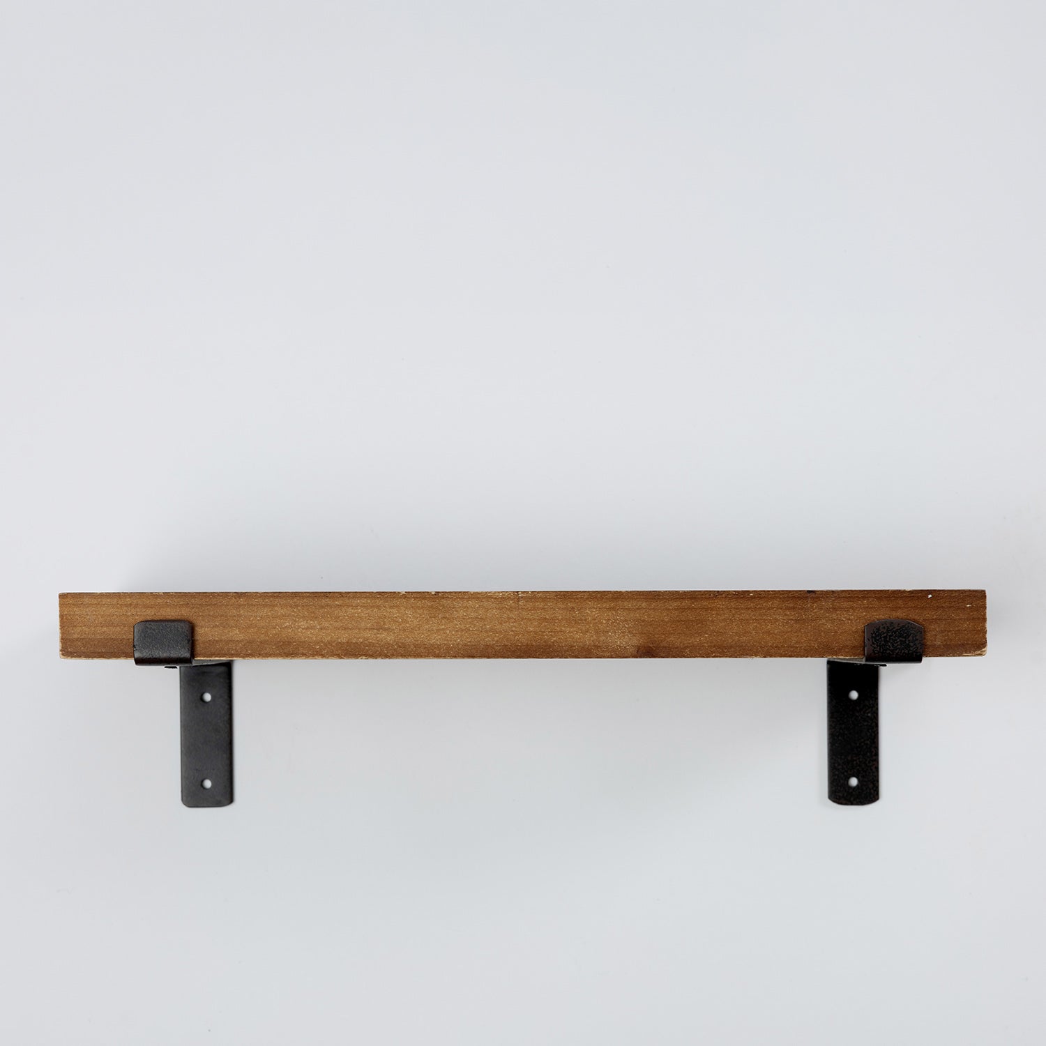 A rustic wooden floating shelf with two black metal brackets, shown against a plain light gray wall.