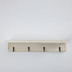 A rustic white-washed wooden wall hook rack with four black metal hooks, shown against a plain white background.