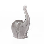Smoke grey hand-blown glass elephant figurine with a raised clear glass trunk, white spotted detailing, and translucent glass ears, displayed against a white background.