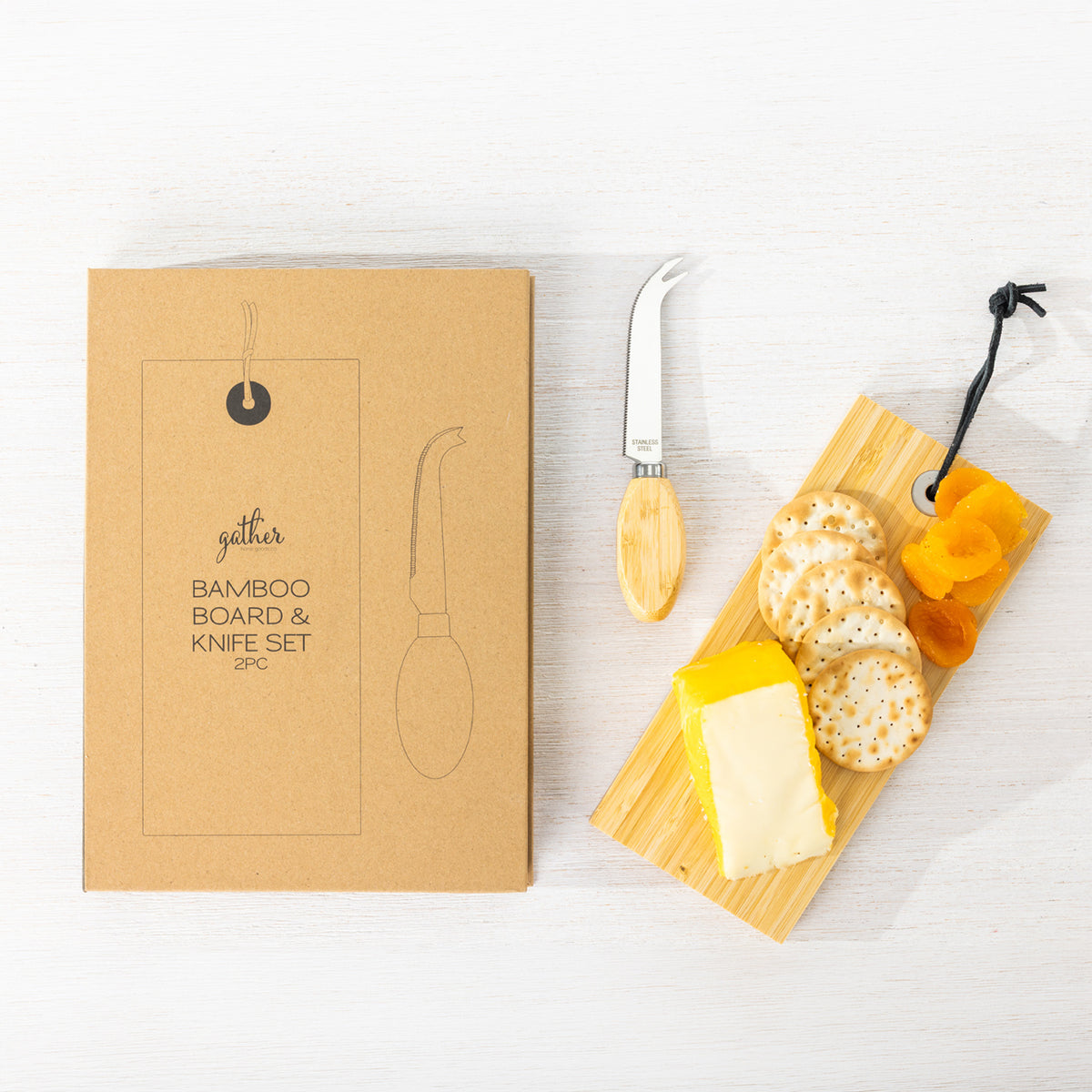 Gather 2 Piece Bamboo Board & Knife Set featuring a natural bamboo serving board with cheese, crackers, dried fruit and a matching cheese knife beside its packaging.