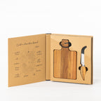 Gather 2 Piece Acacia Board & Knife Set displayed in open gift packaging with a paddle-shaped acacia board and stainless steel cheese knife with wooden handle.