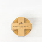 Gather 4 Piece Acacia Coaster Set shown from above with the round wooden coasters stacked beneath branded cardboard packaging.