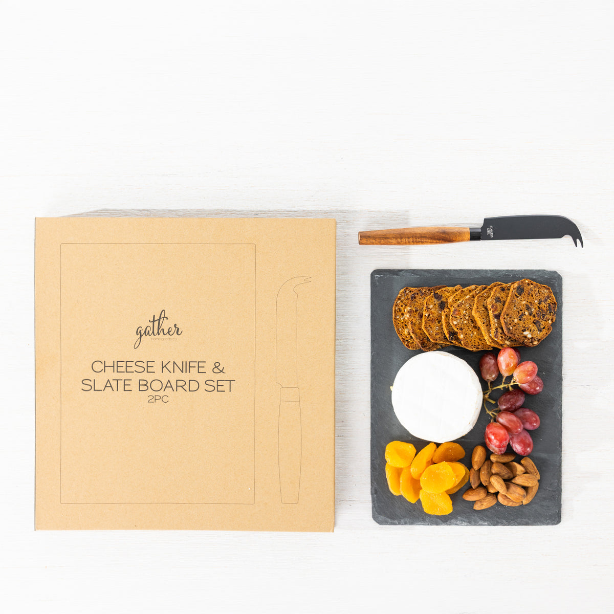 Gather 2 Piece Cheese Knife & Slate Board Set featuring a square black slate serving board with cheese, crackers, grapes, dried fruit and nuts alongside a cheese knife and packaging.