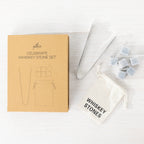 Gather Celebrate Whiskey Stone Set displayed in open gift packaging with six grey whiskey stones, stainless steel tongs and a white drawstring storage pouch.