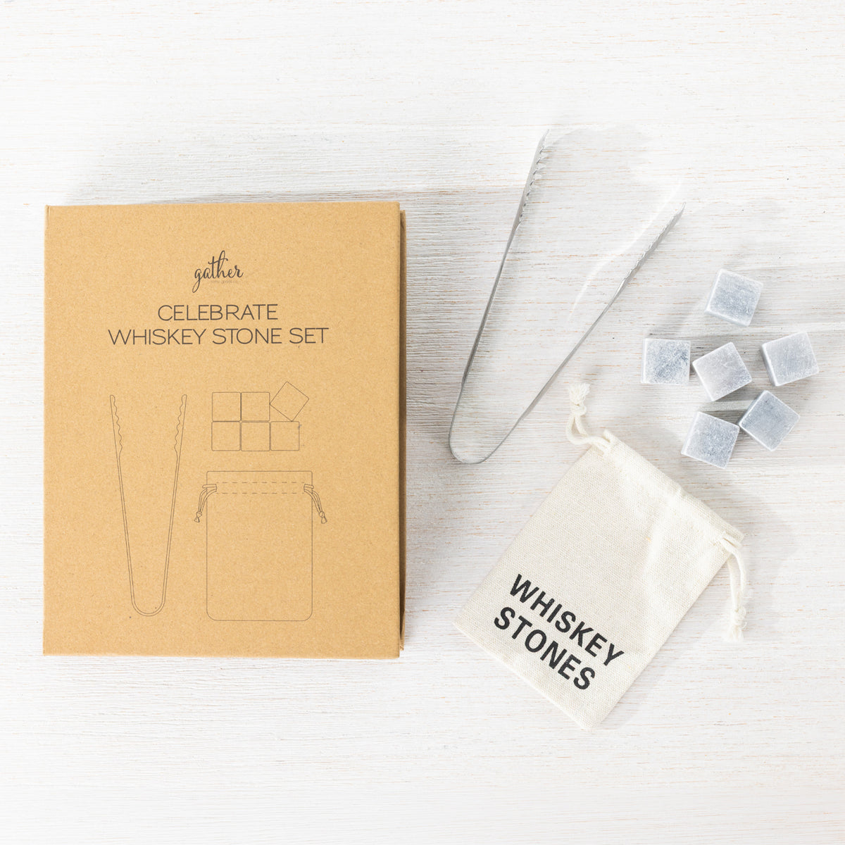 Gather Celebrate Whiskey Stone Set displayed in open gift packaging with six grey whiskey stones, stainless steel tongs and a white drawstring storage pouch.