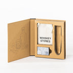 Gather Celebrate Whiskey Stone Set displayed in open gift packaging with six grey whiskey stones, stainless steel tongs and a white drawstring storage pouch.