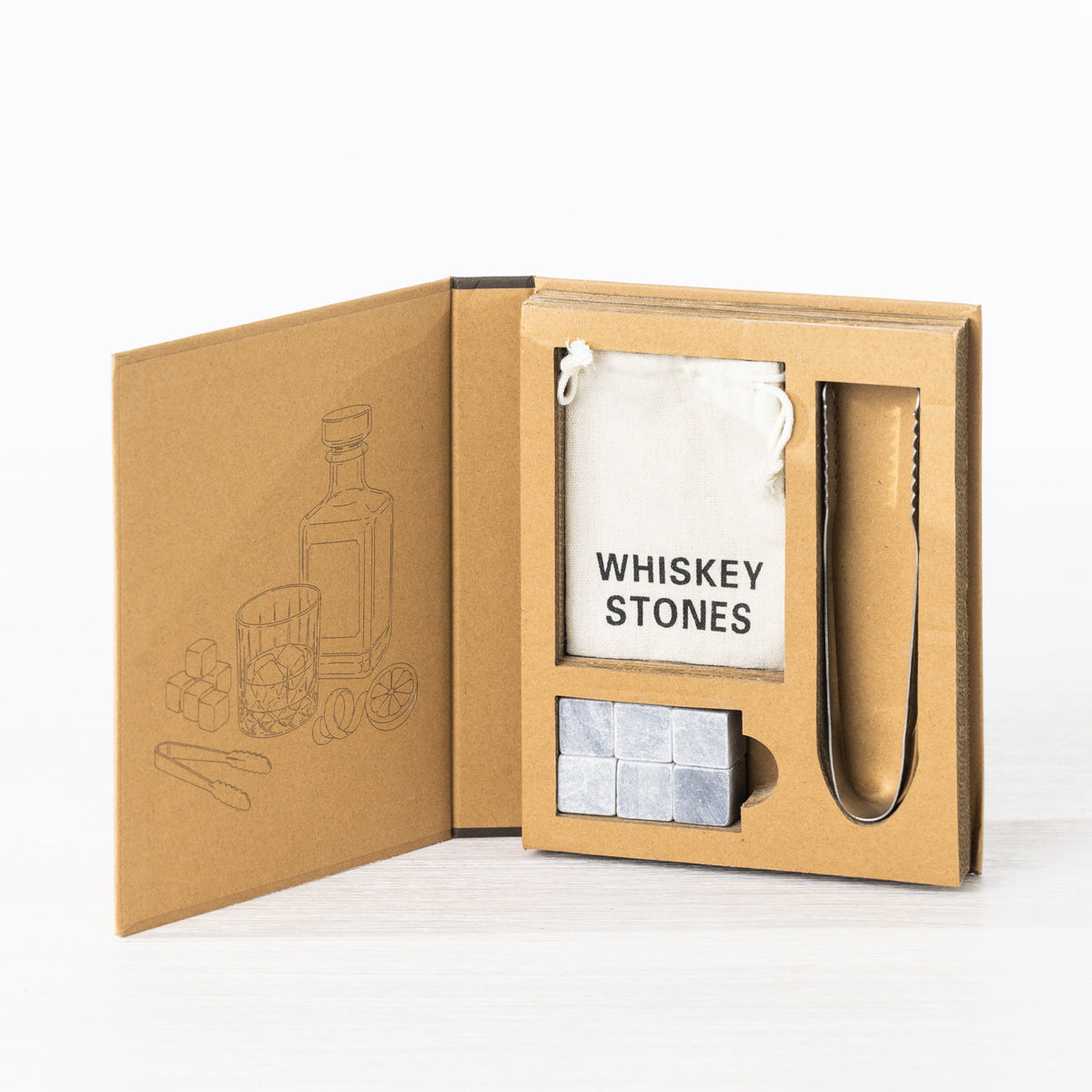 Gather Celebrate Whiskey Stone Set displayed in open gift packaging with six grey whiskey stones, stainless steel tongs and a white drawstring storage pouch.