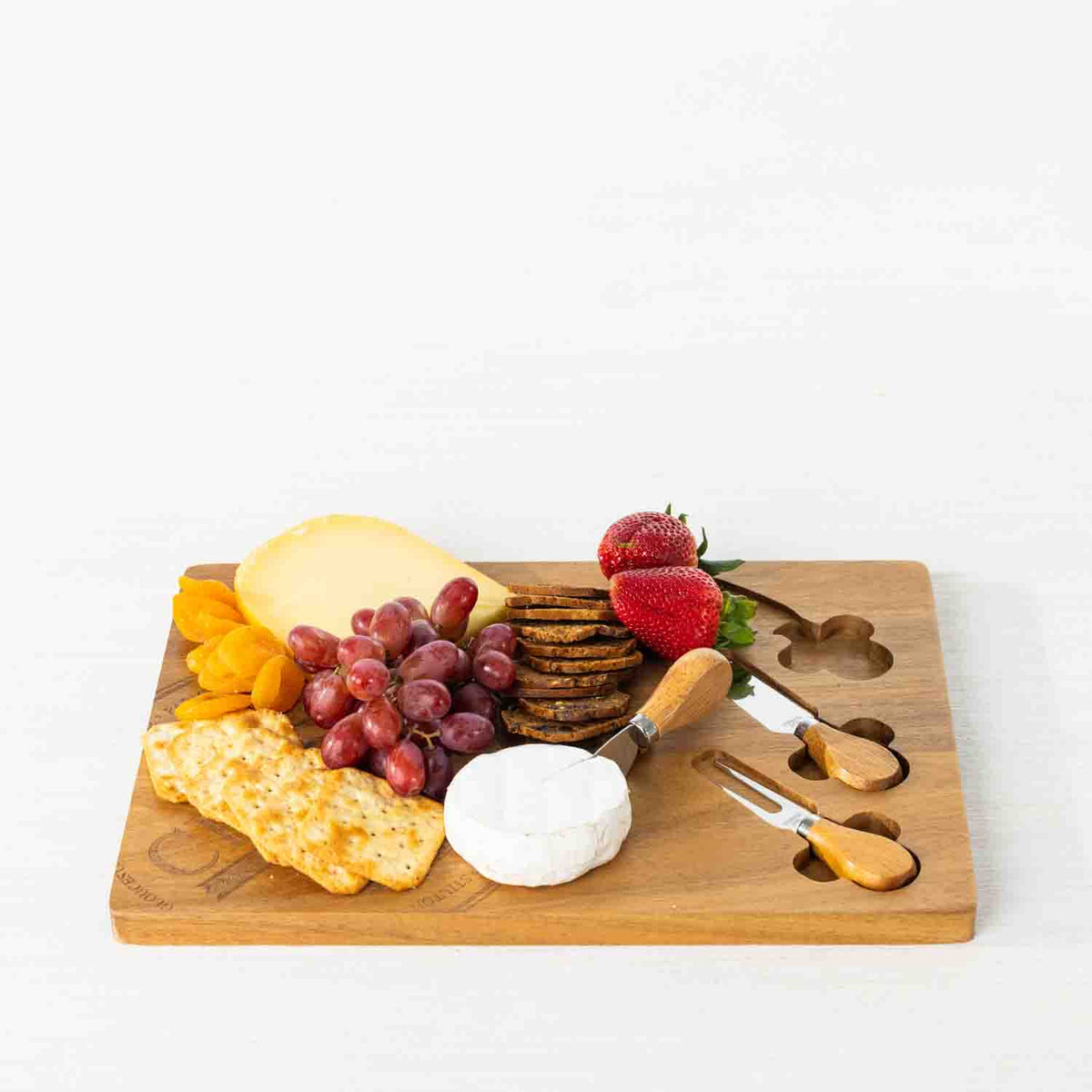 Gather 4 Piece Acacia Board & Knife Set featuring a natural acacia wood serving board styled with cheese, crackers, grapes, strawberries and dried fruit, with three coordinating cheese utensils.