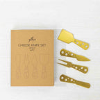 Gather 4 Piece Cheese Knife Set Gold featuring four gold-coloured cheese serving utensils with decorative circular cut-out handles displayed beside kraft cardboard packaging.