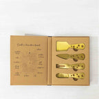 Gather 4 Piece Cheese Knife Set Gold displayed in open gift packaging with four gold-coloured cheese utensils and a charcuterie board illustration inside the box.