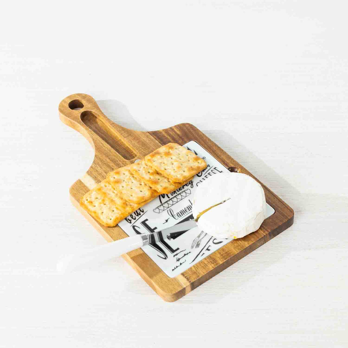 Gather 3 Piece Ceramic & Acacia Set Square featuring a square acacia wood serving board with a decorative ceramic insert, crackers, soft cheese and a white-handled cheese knife.