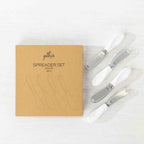 Gather 4 Piece Spreader Set White featuring four stainless steel spreaders with white handles displayed beside the kraft cardboard gift packaging.
