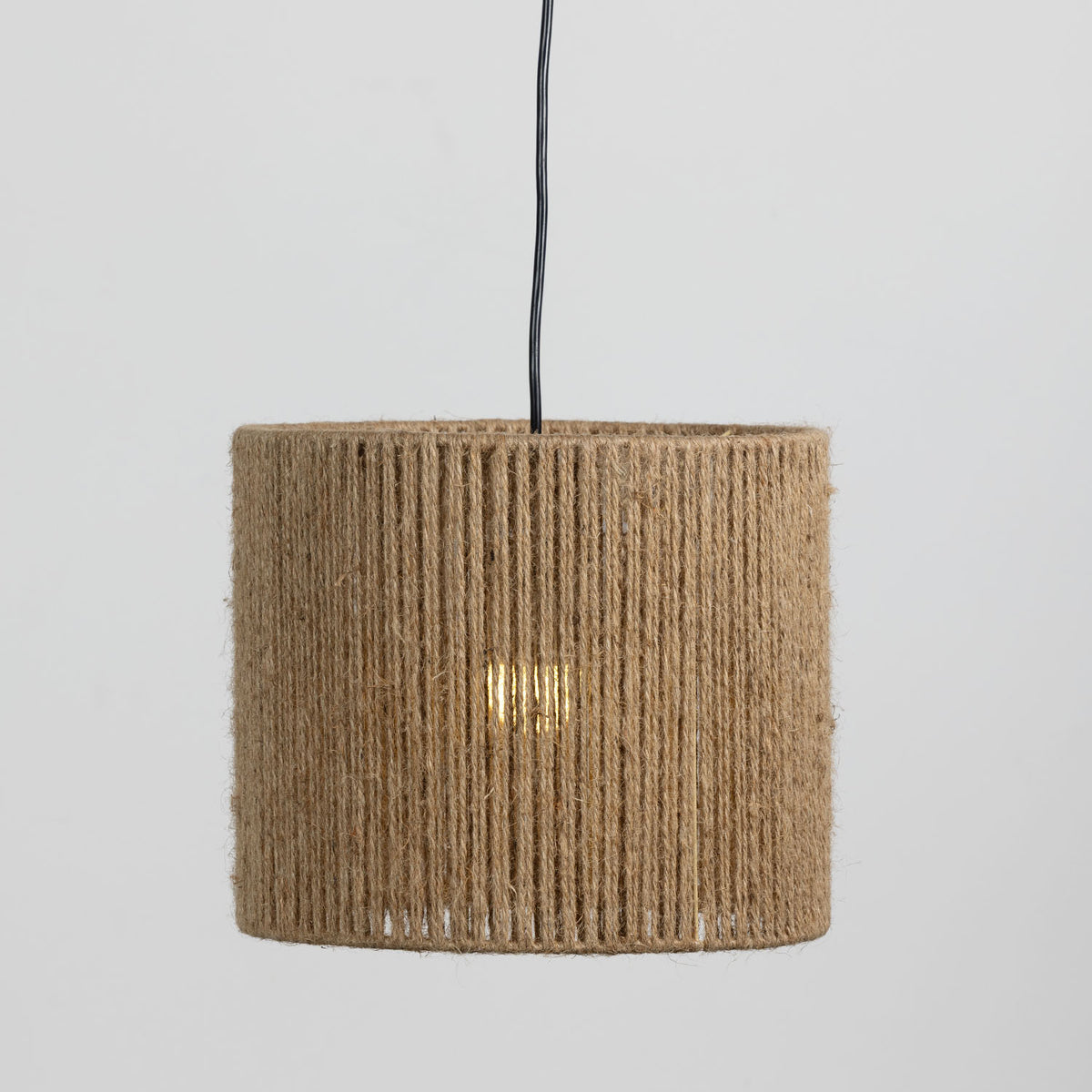 A cylindrical pendant lamp shade made of tightly wrapped natural jute rope, suspended from a black cord against a light gray background.