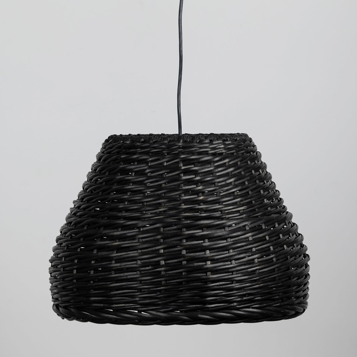 A black woven wicker pendant light shade suspended by a black cord against a light gray background.