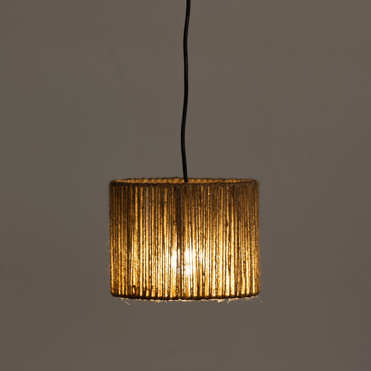 A cylindrical light shade wrapped in natural rope, suspended by a black cord against a plain dark gray background.