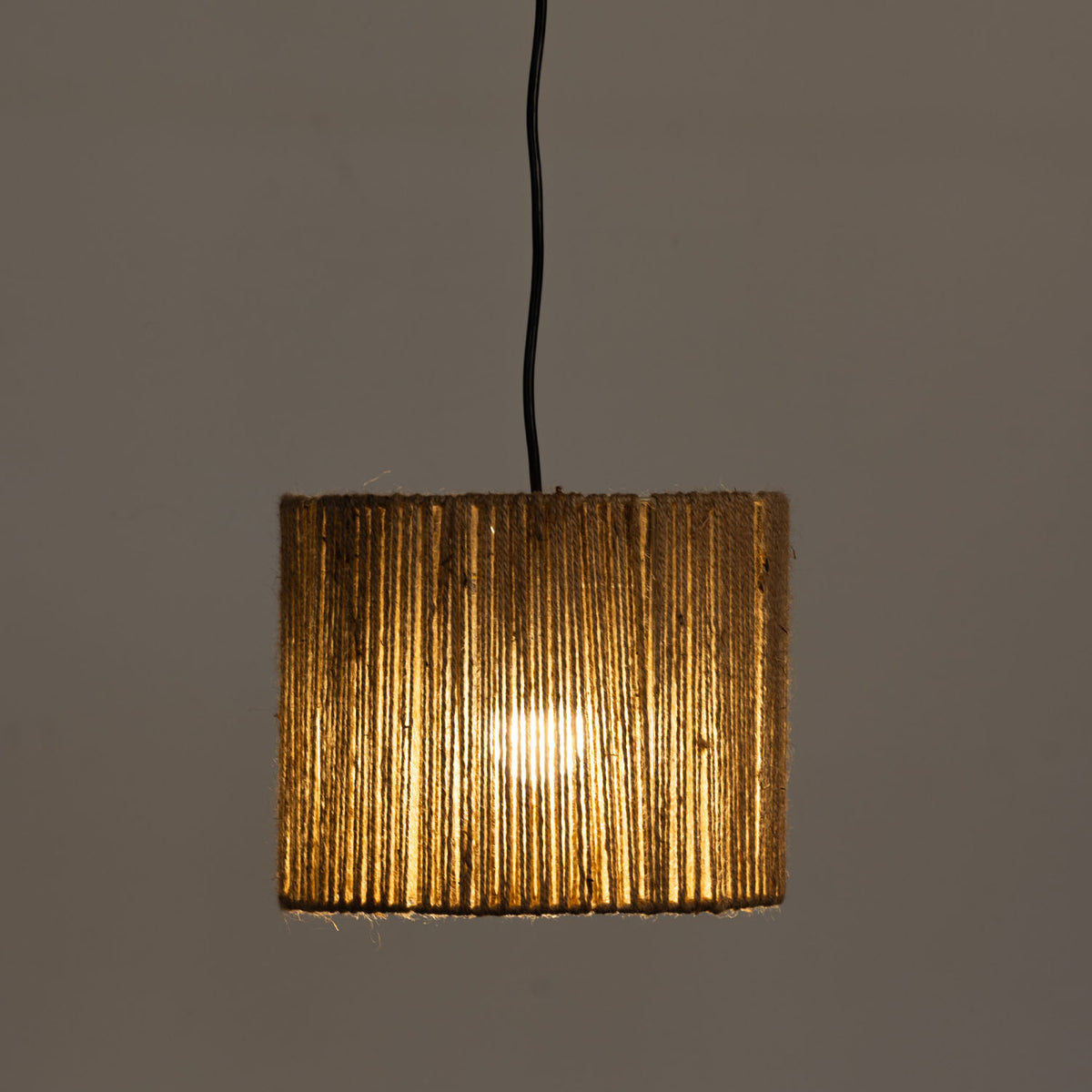 A light shade with a textured, vertically ribbed gold-toned shade, suspended by a black cord against a plain gray background.