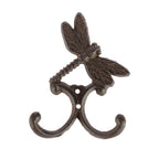A decorative dark metal wall hook featuring a detailed dragonfly above two curved hooks is shown against a plain light background.