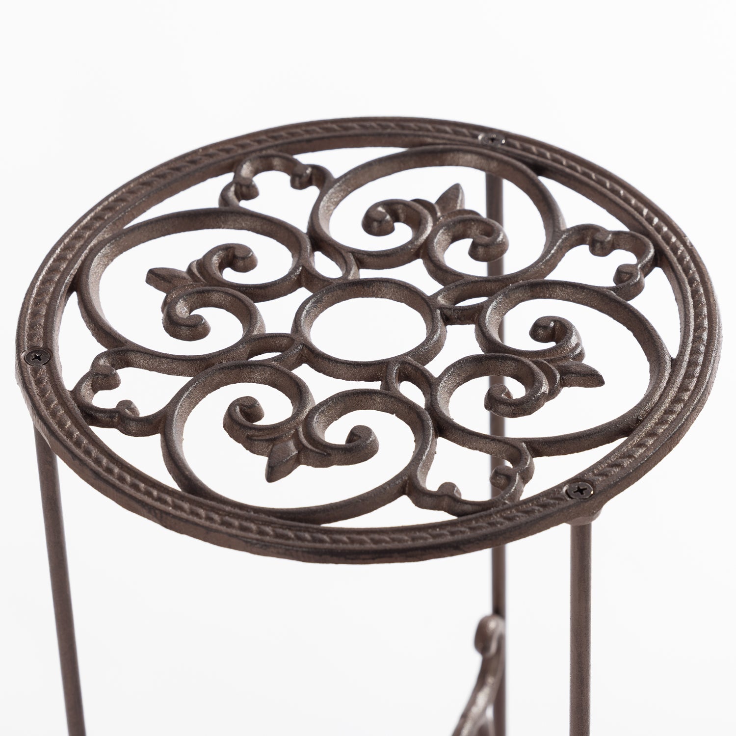 A close-up view of the top of an ornate dark metal plant stand shows an intricate scrollwork design with a circular frame and slender supporting legs against a plain light background.