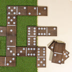 Oversized wooden dominoes arranged in gameplay formation on grass, with additional domino pieces stacked beside the game.