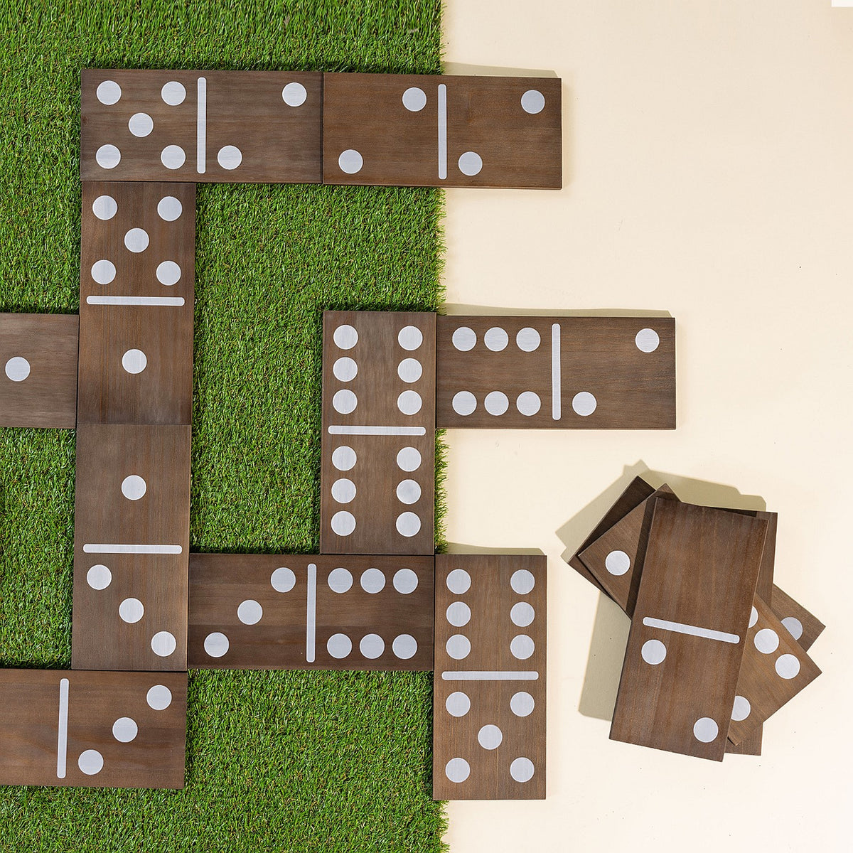 Oversized wooden dominoes arranged in gameplay formation on grass, with additional domino pieces stacked beside the game.