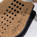 Close-up of a cork paddle featuring perforated detailing and "Play The Field" branding.