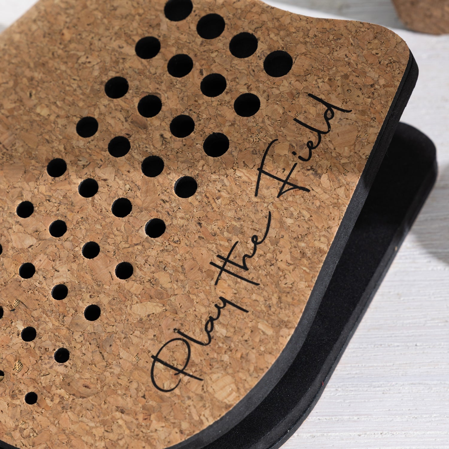 Close-up of a cork paddle featuring perforated detailing and "Play The Field" branding.