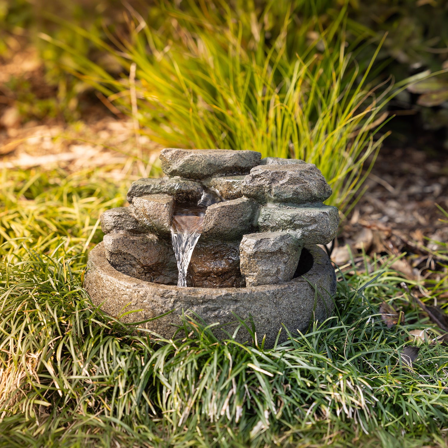 Rock-effect LED water fountain with cascading water, displayed in a garden amongst ornamental grass.