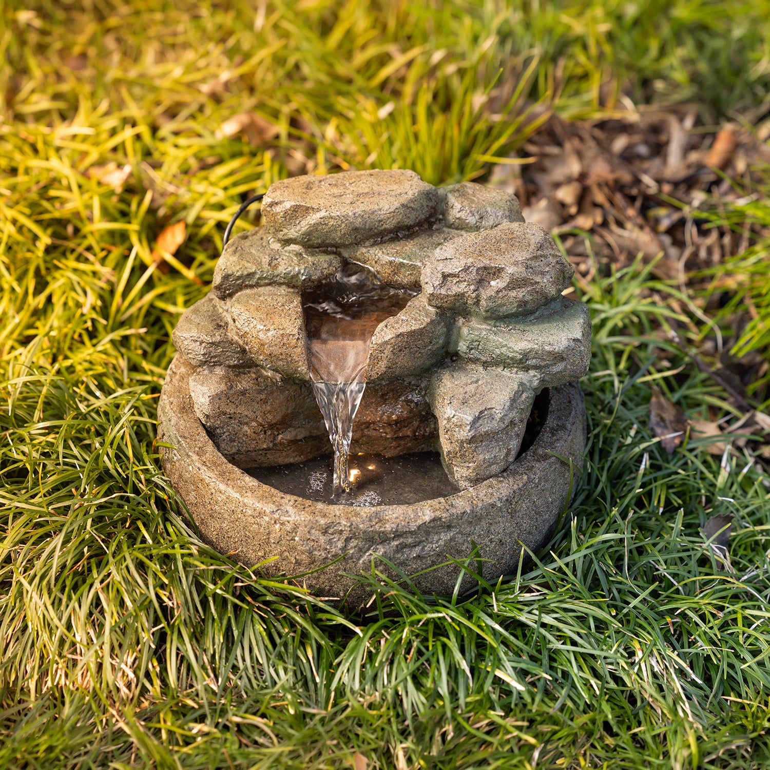 Close-up of the rock-effect LED water fountain in an outdoor garden setting, highlighting the cascading water feature and built-in LED light