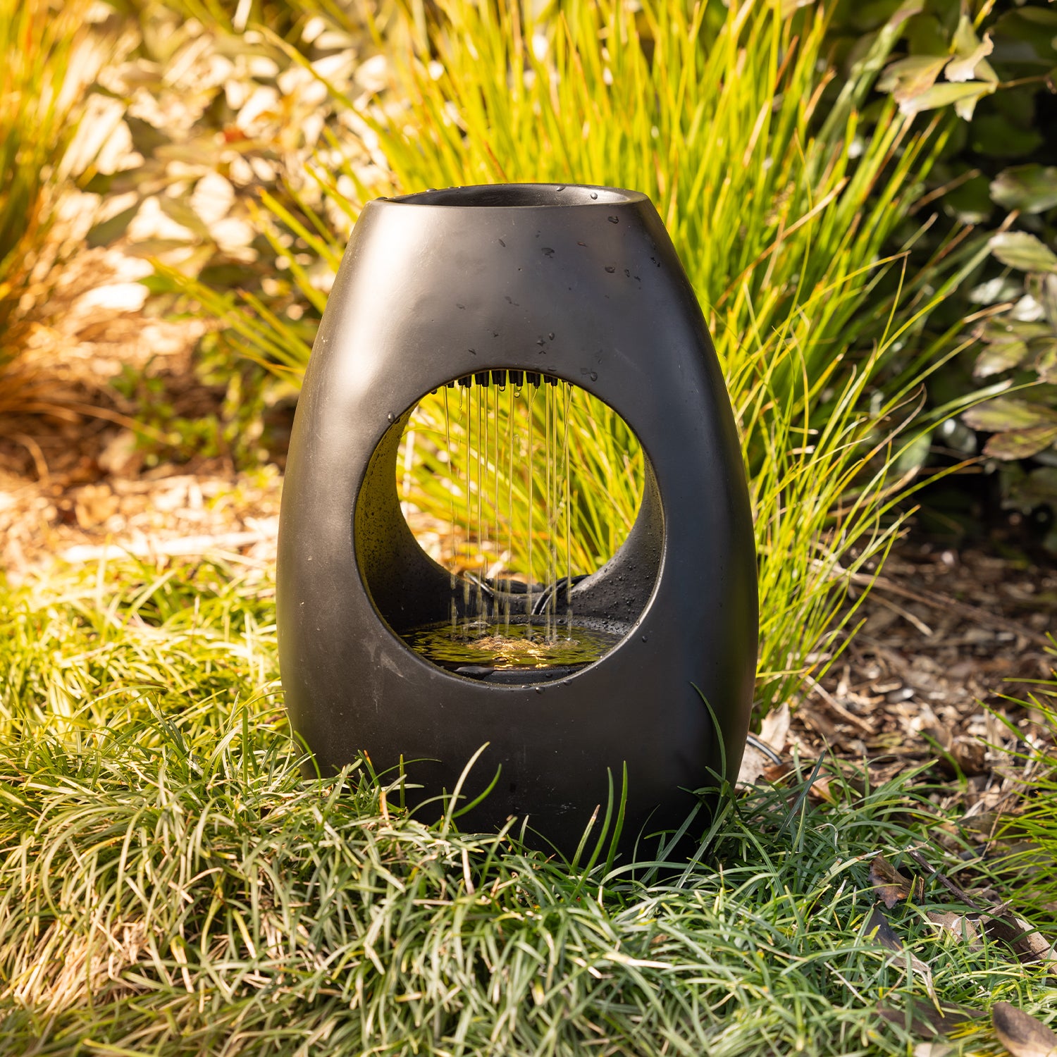 Black rain curtain LED water feature displayed outdoors amongst ornamental grass, showcasing the cascading water effect.