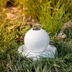 Close-up of the white porcelain ball LED fountain displayed in a garden, highlighting the glossy speckled finish and water feature.