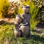 Outsidings Multiple Pot LED Fountain with cascading water flowing between textured stone-look pots, styled amongst lush garden greenery in a sunlit outdoor setting.