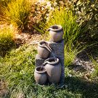 Outsidings Multiple Pot LED Fountain with illuminated cascading water displayed amongst ornamental grasses and garden plants in a landscaped outdoor setting.