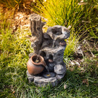 Outsidings Bird & LED Fountain with flowing water and warm LED illumination, nestled amongst ornamental grasses and garden foliage in a natural outdoor setting.
