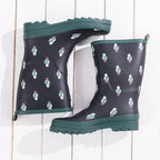 A pair of dark navy rain boots with a repeating pattern of small white and green sheep figures, featuring dark green soles and trim, displayed on a white wood plank background.