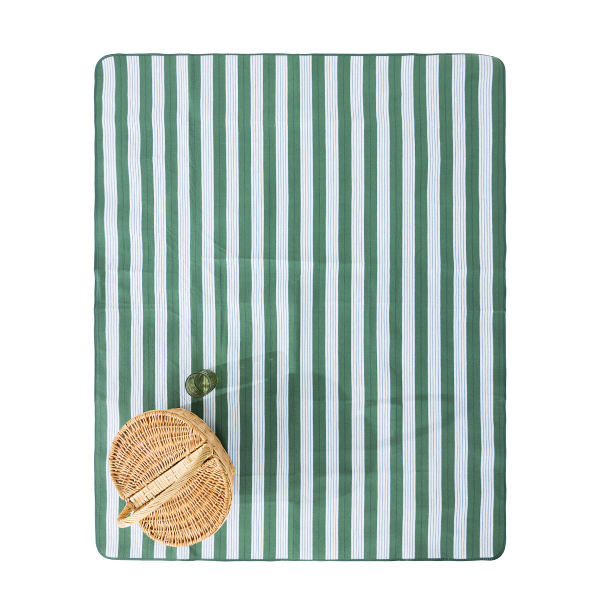 A rectangular green striped picnic mat, styled with a woven oval basket and a green drinking glass on a white background.