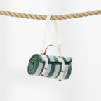 A rolled green striped picnic mat hangs from a thick rope against a clean white background. 