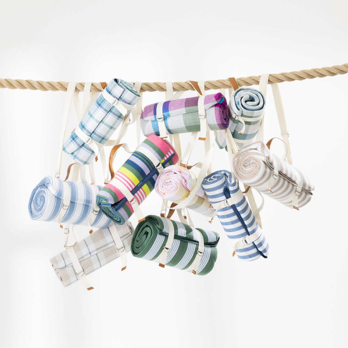 Multiple rolled picnic mats hung from a thick rope against a clean white background. 