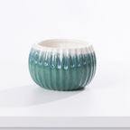 A small round ceramic candle holder with a ribbed exterior, light aqua glaze, and white dripping glaze accents around the rim, shown on a white surface against a white background.