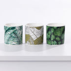 Three ceramic citronella candles with tropical leaf patterns, displayed side-by-side on a white surface against a white background. 