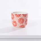 A small ceramic candle holder with a light pink body and a pattern of red daisy flowers, shown on a clean white surface with a soft shadow.