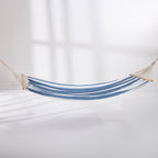 Blue and white striped hammock suspended with wooden spreader bars against a light background.