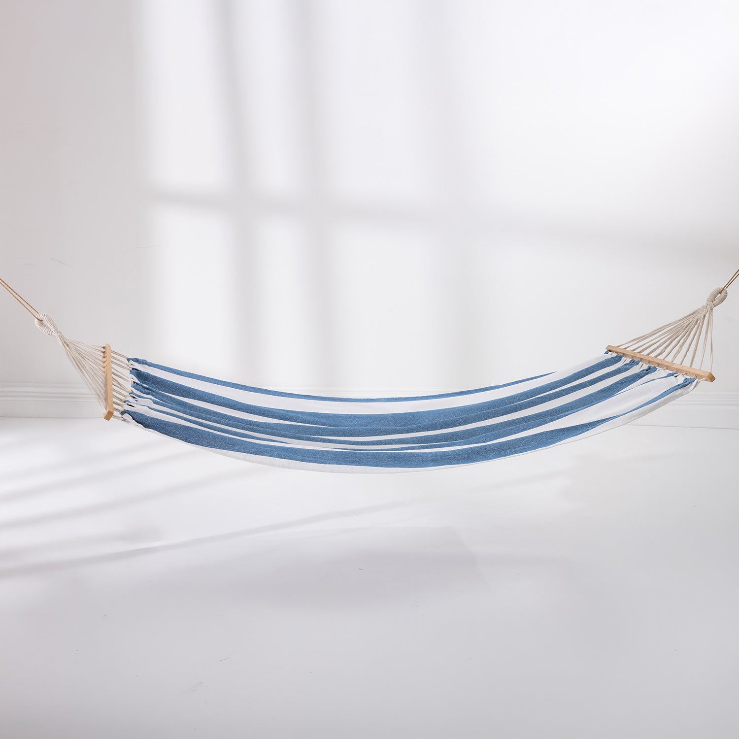 Blue and white striped hammock suspended with wooden spreader bars against a light background.