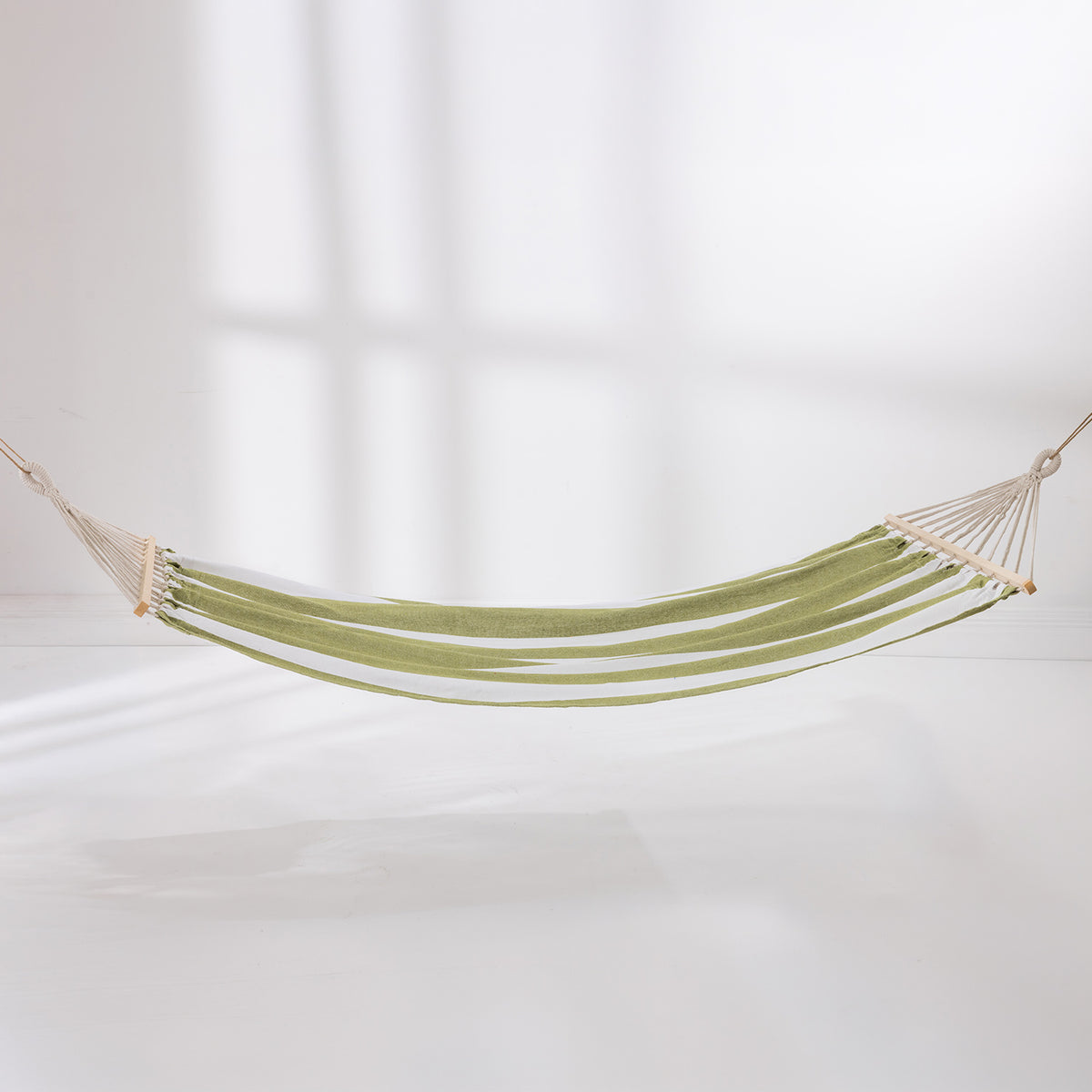 Green and white striped hammock suspended with wooden spreader bars against a light background.